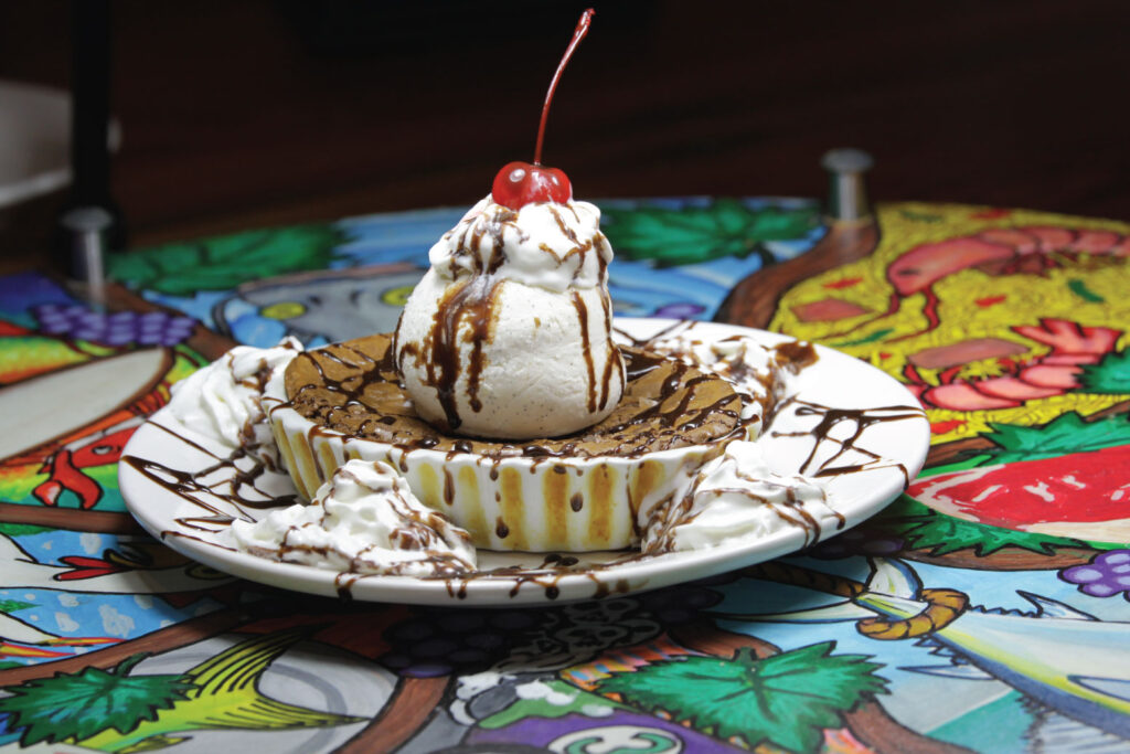 A baked dessert topped with ice cream, chocolate drizzle, and a cherry