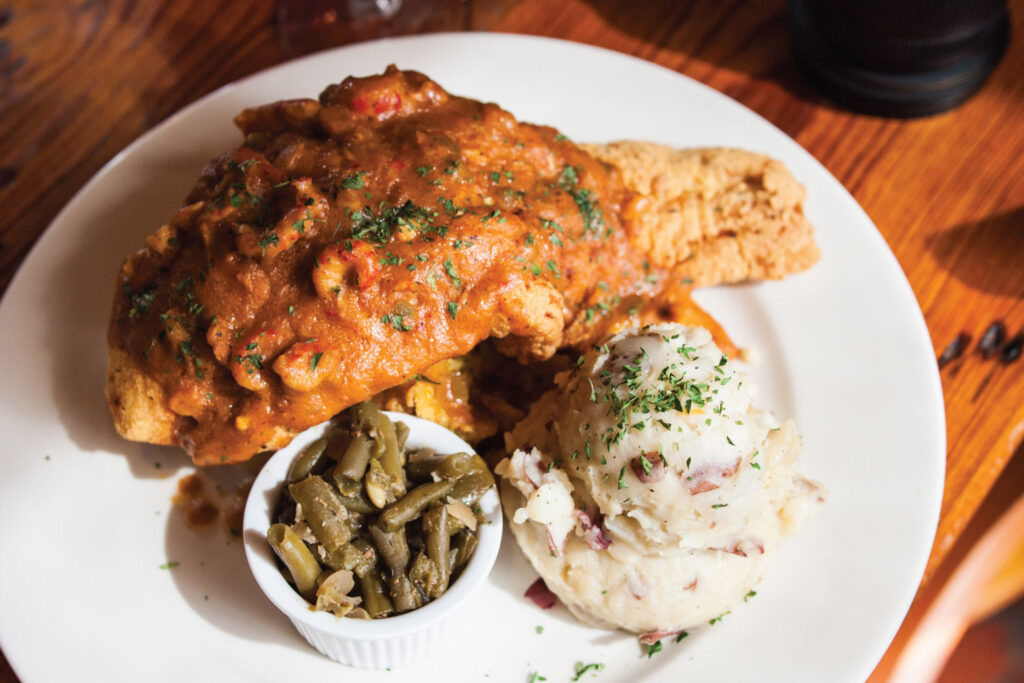 Golden fried fish topped with a rich sauce, with mashed potatoes and green beans